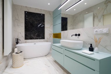 Serbest küvetli, mavi göğüslü, banyo lavabosunun altında mavi dolaplar ve mermer fayanslar olan zarif bir banyo.