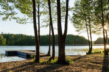 Güzel gün batımı eski, ahşap iskele üzerinde sakin göl üzerinde kum ve çimen kıyısı ile