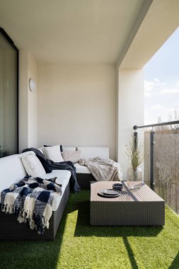 Sahte çimenli rahat balkon ve yastıklı ve kare sehpalı rattan köşe kanepe.