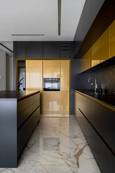 Elegant kitchen with black and gold furniture, kitchen island and marble floor tiles