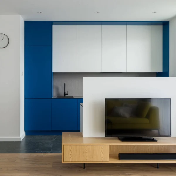 Simple tv room with wooden sideboard open to modern kitchen with white and blue furniture