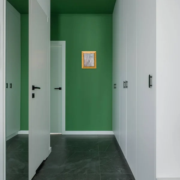 Stylish home corridor with green walls, big mirror, gray floor tiles and white doors and wardrobes