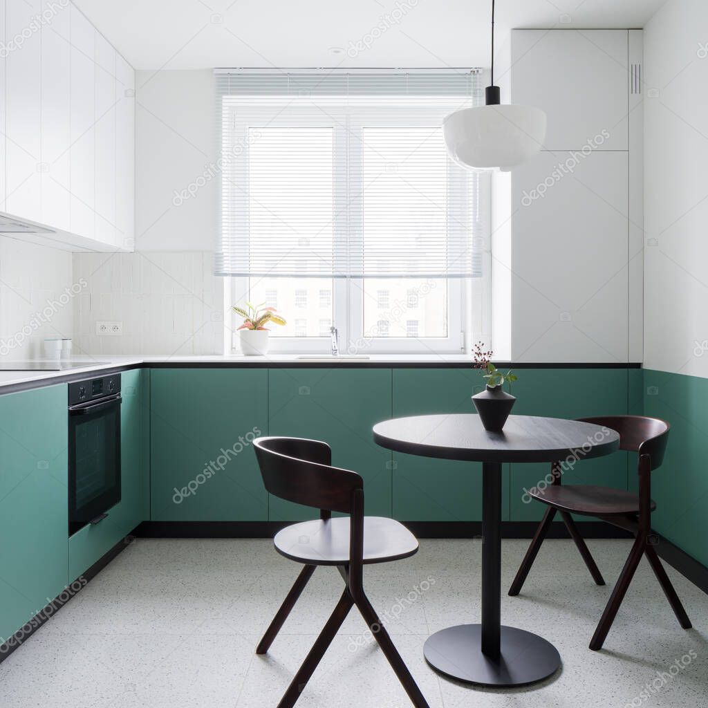 Small and modern kitchen with stylish terrazzo floor, trendy, black dining table with two chairs and stylish white and green walls and cupboards