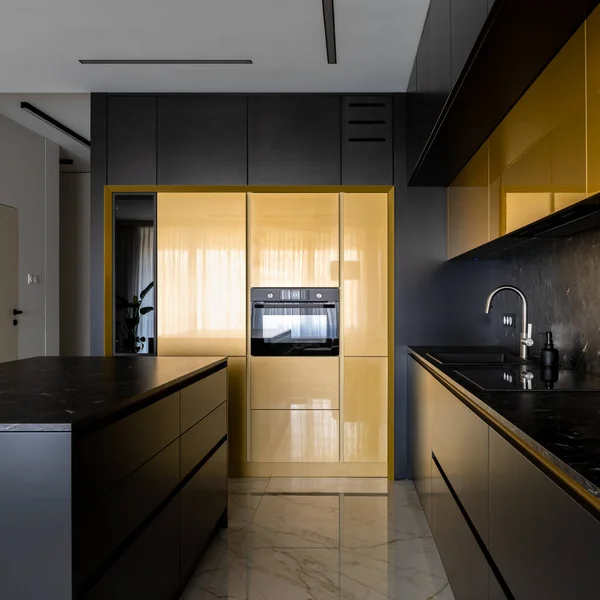 Elegant kitchen with black and gold cupboards and drawers, marble floor tiles and black countertops and backsplash and stylish kitchen island