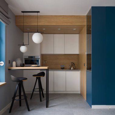 Mutfakta küçük masalı modern ve şık tasarım ve yeni kolye lambaları altında iki sandalye, basit beyaz mobilyalar, ahşap duvarlar ve arka sıçrama, gri döşemeler ve lacivert duvarlar.