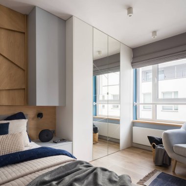 Şık yatak odası, rahat yatak örtüsü, jaluzili büyük pencere ve aynalı kapılı gardırop.