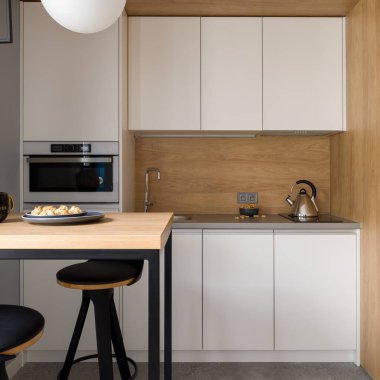 Beyaz mobilyalı küçük ve şık bir mutfak, tahta duvarlar ve iki sandalyeli bir masa.