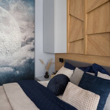 Dekoratif çarşaflar küçük bir yatak odasında, duvarında ahşap bir dekor ve aylı duvar kâğıdı var.