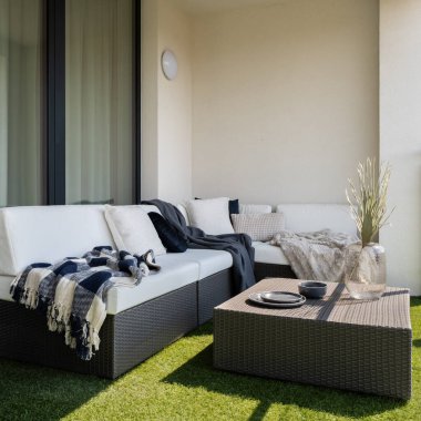 Şık bir balkon, köşeli kanepe, sehpa ve yerde sentetik çimenler.