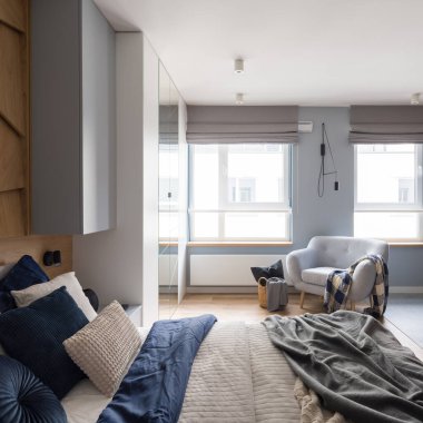 Şık ve parlak yatak odası, rahat yatak örtüleri, yastıklar, büyük pencereler ve rahat koltuklar.