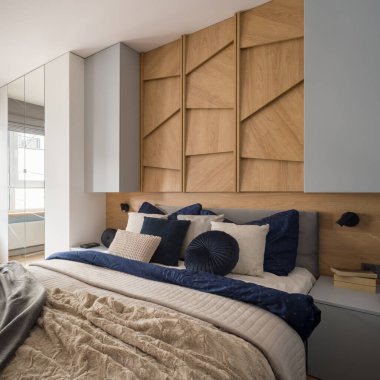 En büyük boy yatak, şık yastıklar, geniş ve rahat yatak odaları dekoratif, ahşap duvarlı, gri komodinli ve dolaplı.