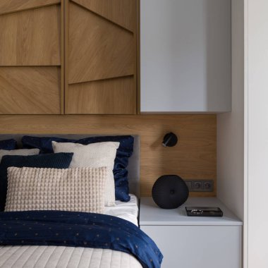 Gri komodinin yanında şık ve rahat bir yatak odası ve duvarında ahşap süslemeler var.