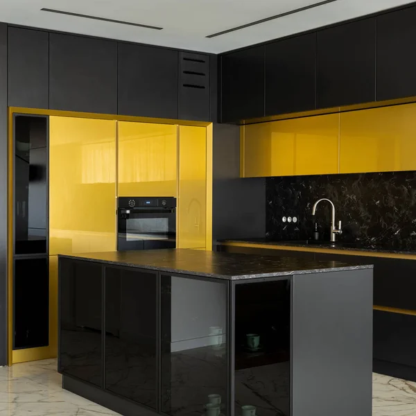 Stylish kitchen with black and gold cupboards and big kitchen island with black, marble countertop