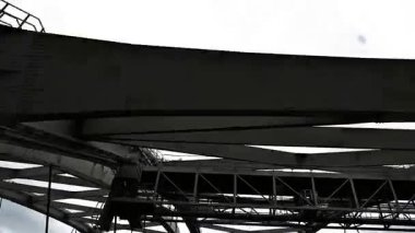 Çarpıcı bulutlu gökyüzüne karşı kesişen kirişleri olan çelik köprünün alçak açılı görüntüsü. Kentsel altyapı, endüstriyel mimari ve geometrik mühendislik tasarım kavramı.