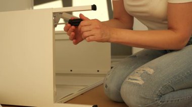 Kadınların elleri tornavidayla düz mobilyaları birleştirirken, tahta zeminde vidayı metal çerçeveye sıkıştırırken. DIY ev geliştirme eğitimi, adım adım montaj süreci