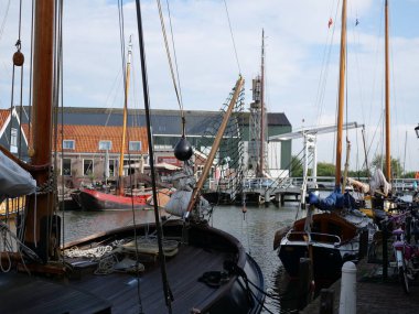 Geleneksel ahşap yelkenli tekneleri, kaldırım taşı kaldırımları, beyaz asma köprüsü ve liman direkleri, yumuşak bulutlu gökyüzü altında sakin su yansımaları olan Hollanda kanalı..