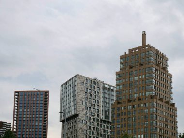 Rotterdam 'da bulutlu gökyüzünün altında çeşitli mimari stil ve malzemeler sergilenen üç modern gökdelenli bina. Çağdaş Hollanda şehir tasarımını yansıtan parlak, kentsel bir ufuk çizgisi.