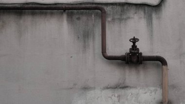 Eski paslı endüstriyel boru ve yıpranmış beton duvarda bir kapı vanası. Demir oksit lekeli, kumlu kentsel çürüme arka planı. Endüstriyel ve grunge tasarım kavramları için klasik tesisat sistemi.