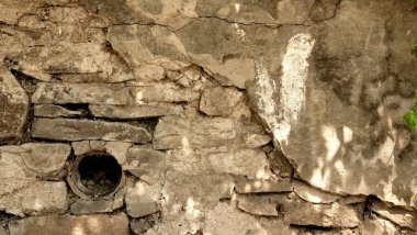 Yuvarlak bir drenaj borusu ve çatlaklar arasında büyüyen küçük yeşil bitkileri olan eski bir kırsal taş duvar dokusu. Eski mimari ve bahçe tasarımı için yıpranmış kireçtaşı mason arka planı.