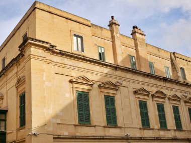 Malta Valletta 'da yeşil, ahşap panjurlu ve süslü pencere kemerli tarihi bir kireçtaşı bina cephesi.