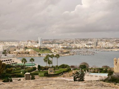 Sayısız beyaz binaları, modern bir gökdelenleri ve palmiye ağaçları ve ön planda bir bahçesi bulunan bir yat marinası olan yüksek açılı bir sahil kenti ve liman manzarası..
