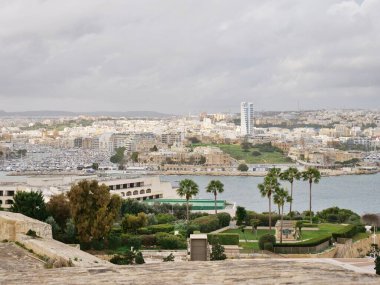 Sayısız beyaz binaları, modern bir gökdelenleri ve palmiye ağaçları ve ön planda bir bahçesi bulunan bir yat marinası olan yüksek açılı bir sahil kenti ve liman manzarası..