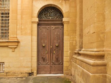 Malta 'nın Mdina kentindeki geleneksel yıpranmış, altından kireçtaşı bir duvarda süslü, eski, ahşap bir çift kapı. Kapıda kemerli demir fanlight ve arması olan barok tasarım elementleri var..