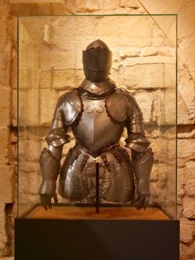 16. yüzyıldan kalma son derece parlak, karmaşık çelikten bir zırhın görüntüsü kaba bir taş duvara karşı cam bir kabın içinde sergileniyor. Zırh, muhtemelen İtalyan tarzında, bir kask, göğüs zırhı, püsküller, gorget ve eldivenler içeriyor.,
