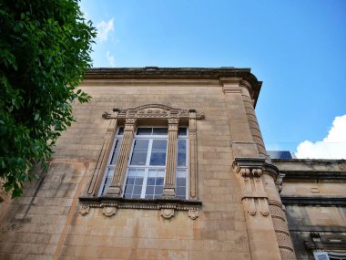 Malta 'da güneşli bir günde mavi gökyüzüne karşı dekoratif sütunlar ve beyaz çerçeveli pencerelerle süslemeli neoklasik kireçtaşı bina cephesi. Bu fotoğraf, tarihsel mimari, gayrimenkul ve Akdeniz seyahatleri için ideal bir stok görüntüsü.,