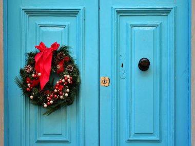 Kırmızı kurdele, böğürtlen ve çam kozalaklarıyla süslenmiş canlı mavi bir çift kapı. Akdeniz 'in Malta adasındaki dikey, güneşli sahne tatil kentsel cazibesini yakalıyor.
