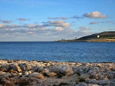 Kayalık sahil sahili ön planda mavi okyanus suyu uzak kasaba binaları güneşli gökyüzünün altında tepe.