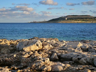 Kayalık sahil sahili ön planda mavi okyanus suyu uzak kasaba binaları güneşli gökyüzünün altında tepe.