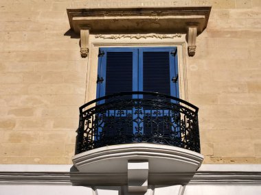 Geleneksel Malta balkonunda mavi ahşap panjurlar ve Malta 'da kireçtaşı bir duvara demirle işlenmiş süslü siyah demirler. Akdeniz mimari ayrıntıları.