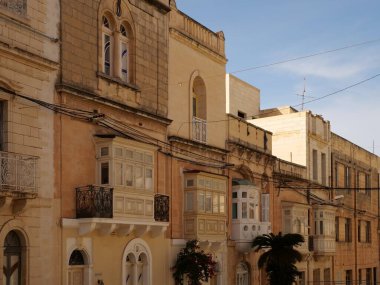 Geleneksel renkli Malta ahşap balkonları Birgu Malta 'nın tarihi kireçtaşı cephesinde gallarija yapıyor. Otantik Akdeniz sokak manzaralı mimarisi