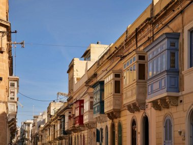 Geleneksel renkli Malta ahşap balkonları Birgu Malta 'nın tarihi kireçtaşı cephesinde gallarija yapıyor. Otantik Akdeniz sokak manzaralı mimarisi