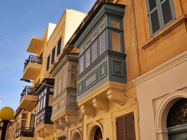 Malta 'daki tarihi kireçtaşı binasının ön cephesinde geleneksel mavi Malta ahşap gallarija balkonları. Açık gökyüzü altında Akdeniz mimari sokak görüntüsü.