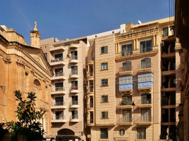 Birgu, Malta 'daki St. Anne Tarihi Kilisesi. Geleneksel kireçtaşı mimarisi. Dar bir sokakta mavi ahşap gallarija balkonları ve modern daireleri var.