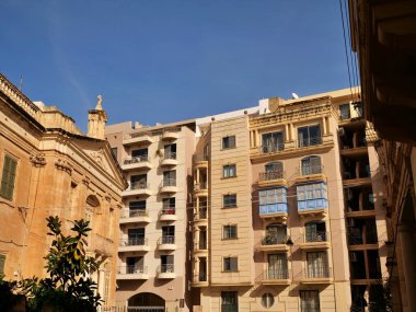 Birgu, Malta 'daki St. Anne Tarihi Kilisesi. Geleneksel kireçtaşı mimarisi. Dar bir sokakta mavi ahşap gallarija balkonları ve modern daireleri var.