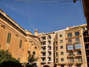 Birgu, Malta 'daki St. Anne Tarihi Kilisesi. Geleneksel kireçtaşı mimarisi. Dar bir sokakta mavi ahşap gallarija balkonları ve modern daireleri var.