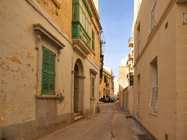 Geleneksel kireçtaşından evler ve yeşil ahşap gallarijabalcony ile Malta 'da dar bir sokak. Mavi gökyüzü altında otantik Akdeniz şehir mimarisi