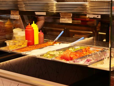 Düsseldorf, NRW Almanya - 13 Şubat 2026: Düsseldorf Havalimanı 'ndaki Taze salata barı ve baharat standı (DUS). Dilimlenmiş domates, salatalık, soğan, ayvar ve yoğurt sosu içeren metal tepsiler..