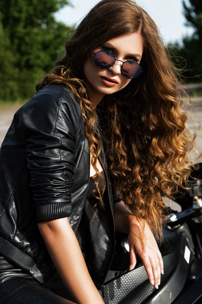 Mujer motociclista sexual con chaqueta de cuero negro con su motocicleta deportiva en una carretera. Belleza, moda. Aventura y libertad . — Foto de Stock