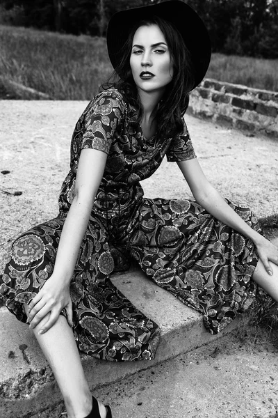 fashion outdoor portrait of a beautiful brunette woman dressed in a suit and a black hat in the field. Black and white