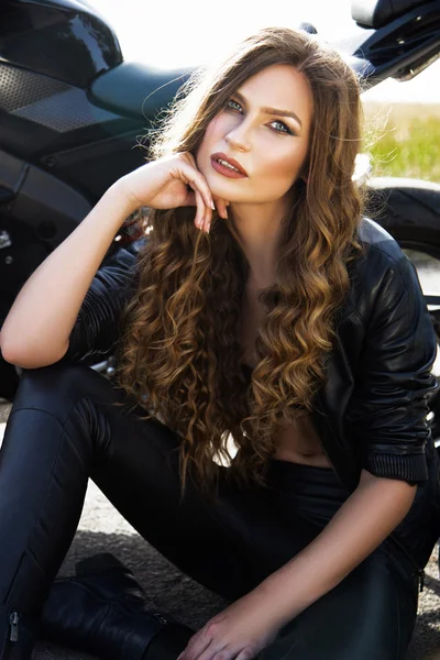 Mujer motociclista sexual con chaqueta de cuero negro con su motocicleta deportiva en una carretera. Belleza, moda. Aventura y libertad . — Foto de Stock