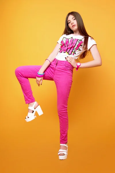 Güzel bir 13 yaşında kız pembe pantolon ve sarı arka plan üzerinde stüdyoda bir t-shirt giymiş — Stok fotoğraf