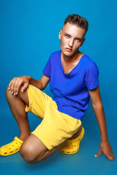 Vertical full length portrait of young man in casual clothes sitting on blue background — Stock Photo, Image