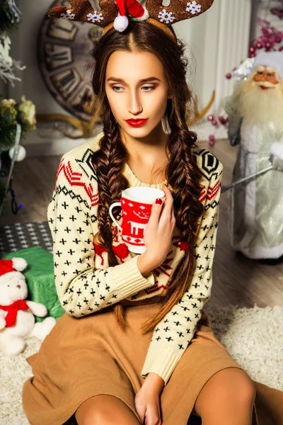 Beautiful girl near a Christmas tree sitting with a cup in her hand — Zdjęcie stockowe