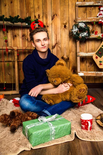 Przystojny facet siedzący z niedźwiedzia zabawek w sali z ozdób choinkowych. Nowy rok — Zdjęcie stockowe