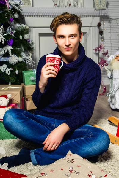 क्रिसमस के पेड़ के पास कमरे में एक कप के साथ सुंदर आदमी। नए साल की अवधारणा — स्टॉक फ़ोटो, इमेज