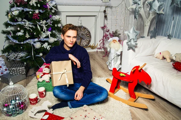 Um tipo bonito a segurar um presente na sala perto da árvore de Natal. Conceito de ano novo — Fotografia de Stock